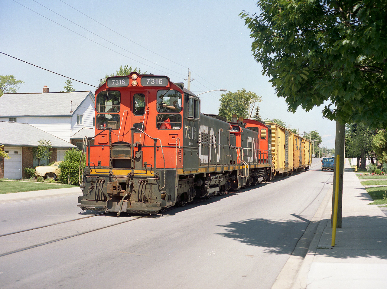 CN 7316 and 7305 trundle down the middle of Pine St in Thorold in August 1999 with what was apparently the last run to the Gallagher paper plant farther up the street near Albert Av. Three boxcars were retrieved from the plant, which had declared bankruptcy 2 months previously, and closed in August'99. The recycled paper operation was known as Noranda Forest, Inc until taken over by Mike Gallagher operations in 1997. The plant was offered for sale and speculation that it might return to operations under a new name never materialized. For me, this was the ultimate in luck to happen by at this time. So for the record, this trackage was never operated by the Port Colborne Harbour (Trillium), which was in the process of taking over St. Catharines area switching.