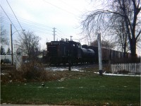 A long time back I had a really lousy little camera, a square shooter no less, and the very worst was to take a lousy camera out on a lousy day and see something good. And this happened. I had lost my old "Hawkeye" a couple years previous and still had not saved for a replacement of decent quality. So this image is the best I could do this day, despite one of the dedicated members of this group enhancing the image you see. I consider this a rare shot. CN 1227, one of the fleet of SW1200RS units, is seen pulling a lone tank and a string of boxcars up from the commercial establishment down by todays' Confederation Park in Stoney Creek. The Beach Line used to run from a connection with CN at Lake St, Stoney Creek, over the Traffic Circle, all along the beach and up to a connection with the CN main at Burlington (West) junction. When the Circle was replaced with the modern interchange at Centennial Parkway in 1969-70; the line became just an industrial run to what I remember as Langs Frozen Foods; the building still exists on the north side of the QEW between the Pwy and Burlington St exit.
In this view, taken from Elgin St looking toward Lakeshore Rd, one can see Brock St in the background, the business structure still there today. This track is long gone, and is a parking lot for an apartment building since constructed just off to the right in the photo. The line used to be busy, a passenger/freight station existed in close proximity around 75 years ago. The fact trains ran thru here once is almost all forgotten. (I wonder what happened to that nice concrete Whistle sign?)