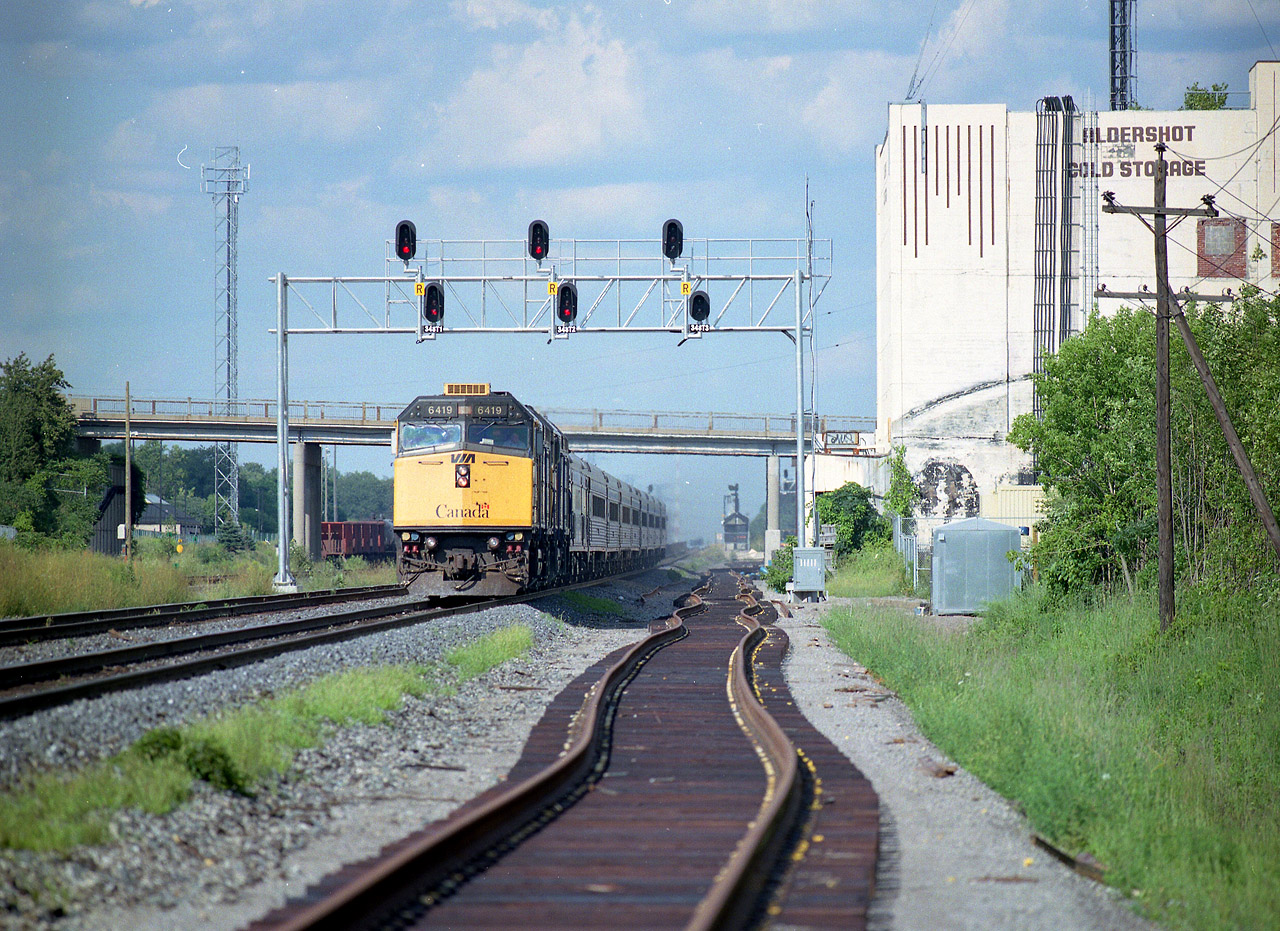 Looking east towards the scene of Marcus Stevens' recent 'off the bridge' Aldershot image (#28049); and this shows the beginning changes that he speaketh of. The former maintenance access is now taken up by new track laid in place for the ambitious "Third Track" project at the time,in order to accommodate future GO Transit traffic. A new overhead signal bridge is now in operation. And the late afternoon VIA #75 is moving smartly along behind VIA 6419 and 6421, unlike the old long and majestic passenger trains I remember when first getting in the hobby. Past Marcus' vantage point off the bridge, you can barely see the platforms for Aldershot Station. Ironically enough, there used to be a signal bridge many years ago very close to where this new one is. And the landmark Cold Storage building and its siding is but a memory.