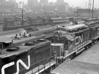 Canadian National's Spadina Yards and surrounding area in downtown Toronto was always a hubbub of activity dating back to the steam era. This 1970 view of the Spadina roundhouse and engine servicing facilities shows a great variety of power that was typical for CN back in the day, as well as some other goodies:<br><br>In the foreground are CN's only two GP35's, 4001 and 4000 (the long hood of which is visible on the lower left) coupled to an MLW RS18. Parked on the next track over is a 1900-series GMD1 (equipped with steam generator and B-B trucks) facing an Ontario Northland 1500-series FP7 and CN FPA4 (likely both together for service on the old "Northland" passenger train that pooled ONR & CN equipment). CN "Railiner" RDC cars are visible on the next track, with one in the background coupled to a pair of GP9's (4130 and 4147, the 4100-series units were equipped with steam lines for use in passenger service).  Behind them are four more 1900-series GMD1's, and some MLW S13 switchers used for switching the coachyard (one appears to be coupled to a slug - possibly a visiting hump set from MacMillan Yard?). Steam generator cars populate many of the stub tracks around the roundhouse turntable<br><br>Visible by the main Toronto Terminals Railway tracks leading to and from Union Station in the background are CP container flatcars (6-axle trucked flats converted from old heavyweight passenger cars) loaded with early 20' containers, the TTR's John Street interlocking tower, and CN 40' boxcars lining the platforms and team tracks used by various customers to load and receive deliveries downtown (like newsprint - as evident by the yellow-doored boxcars mixed in. The Toronto Daily Star, Toronto Telegram, and Globe & Mail were known customers).<br><br>The early 70's era Toronto skyline is also visible, including the ever-present CPR Royal York Hotel, the "new" Toronto-Dominion Bank Towers built in the mid-late 60's, the CN Telecommunications building at 151 Front St. (later becoming CNCP Telecommunications, and then Unitel). And, the top of Union Station and the old CN Express building (converted into the Skywalk in the 80's) are visible just above CN's Spadina Roundhouse at the upper right (which was demolished in the mid 1980's for construction of the Skydome).
