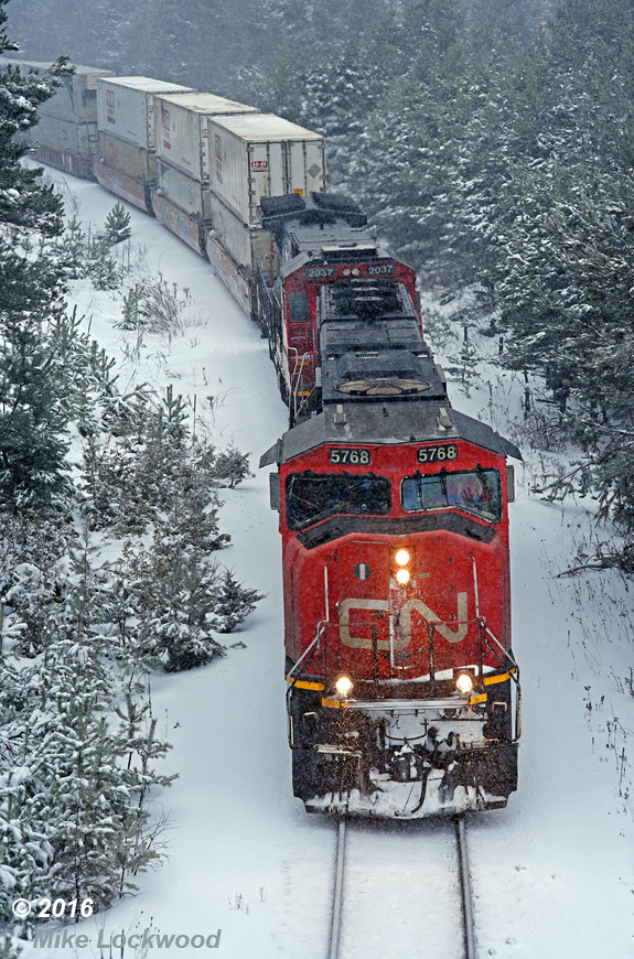 Grinding upgrade in the midst of a decent snowfall, CN 5768 and 2037 lead 106's train through the hairpin curve just north of the north home signal Pine Orchard. 1508hrs.