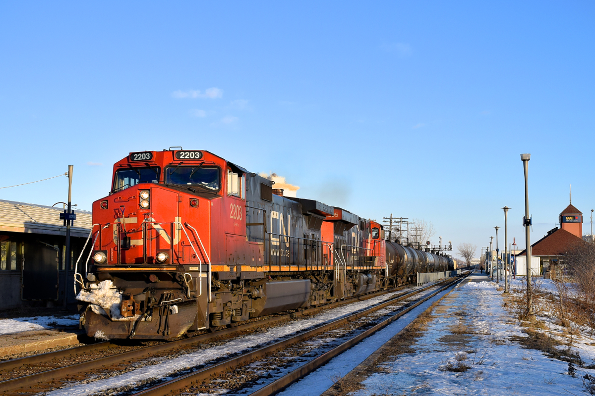 CN 2203 & CN 2295 lead CN 377 past the VIA Dorval Station on a sunny afternoon. At left is a small portion of the parallel AMT Dorval Station.