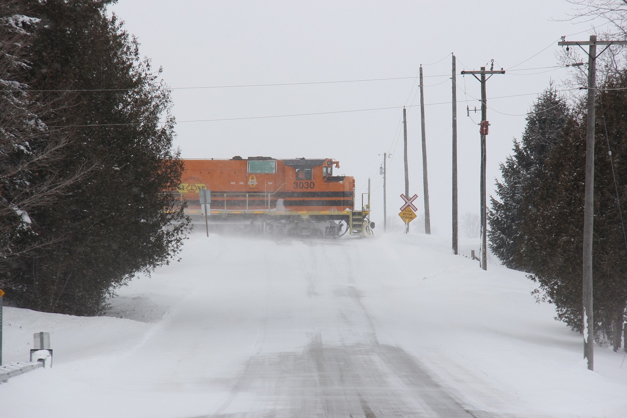 I recall a recording of Christmas Specials from when I was a child, and in between were commercials from the late 1980s. One commercial, about selling snowmobiles, had a line in it, "it's winter in Paul Sadlon country." Well, that's near Barrie. But this is another Ontario snowbelt location, near Hensall, Ontario in "Ontario's West Coast." Appropriately named as it is the region in Ontario just east of Lake Huron, another snow machine in the winter months. 

It is one week until Christmas, and the scene is very representative of those classic Christmas winter scenes. There is an exception. Those orange and black locomotives of parent G&W. This is GEXR during a lake effect snow period. Trumbling along the GEXR Exeter Sub, light power, is GEXR 581 on its way to Stratford to end their day. Here it is pictured crossing Kippen Road just outside the community of Kippen.