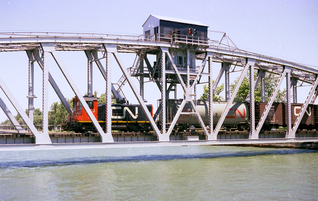 In somewhat of a response to Glenn Cherry's recent submission showing TRRY 1859 rolling along trackage that was newly laid in 1997 and the canal bridges in the background, I decided to dig up a shot of a train on that former lift-style Bridge 20. Unfortunately back then it was dicey at best to try and drive over bridge 21 to give chase, but rather follow the train on foot. And that was no piece of cake either. I did manage one shot on each side of the bridge plus this image taken as it is crossing westbound. But back then, with no zoom lens available, this was as good as it got. Pictured is CN 7166, returning to Port Colborne from Nickel, as indicated in an old CN timetable. The switcher is an SW8, built 1951 and whole series gone by 1989. I must have looked like some sort of deranged nut running around out there on a HOT day, but, well, we all have our weird habits.:o)