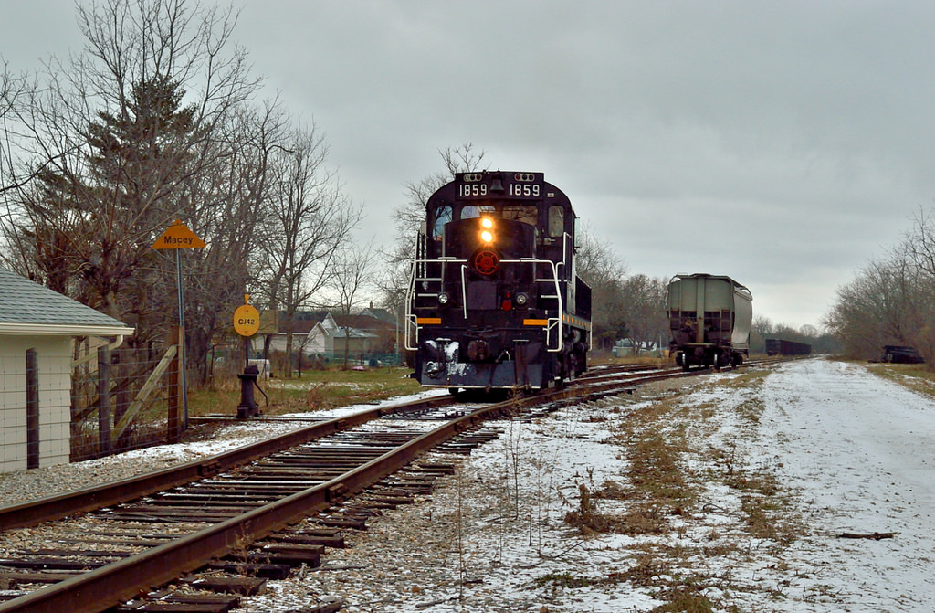 Trillium Ry. 1859 stops and waits for the conductor to throw the switch.  1859 just dropped the car in the siding, has run around it, and is lifting it for the trip to the Port Colborne Grain Terminal.Originally laid through Port Colborne in 1853 by the Buffalo, Brantford & Goderich Railway, the Dunville Sub came under control of the GTR, in turn becoming the CNR in 1923.TH&B built their own Dunnville Sub from Smithville, ON through Dunnville to Port Maitland on the shores of Lake Erie.  The TH&B wished to access the industries of Port Colborne and gained running rights in 1927 over the CN Dunnville Sub from approximately mile 37.42 to about mile 19.65, where TH&B trains would turn south on what is now the Trillium Railway Government spur and head to the Port Colborne Grain Terminal and ADM Milling.TH&B running a rights were still used in 1987 (60 years since first obtained) when TH&B was amalgamated into CP Rail.  In 1988 the running rights were not renewed, and TH&B in Port Colborne was finished.Today, there is a laneway running parallel to Clarence Street and Charlotte Street, it sits between the two streets.  It is to access the rear parking lot of the TD Canada Trust bank.  Immediately behind the bank the TRRY Government spur crosses this lane.  One of the cross bucks is mounted on a wooden post.  On the rear of the post, under reflective striping, sits the lettering; TH&B Ry.I wish I could have found more history of the operations of Port Colborne and Macey Yard, but this is all.  If anyone knows anything of these lines, please leave in the comments.