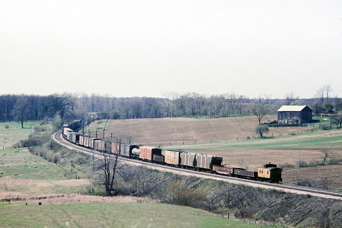 Who said the CASO Sub (Michigan Central) was straight.  A Short C&O freight is westbound at Clanbrassil, ON. back in the days when a crummy brought up the tail end. This westbound freight has passed under the wooden farm access bridge and is traversing the sweeping S-curve.