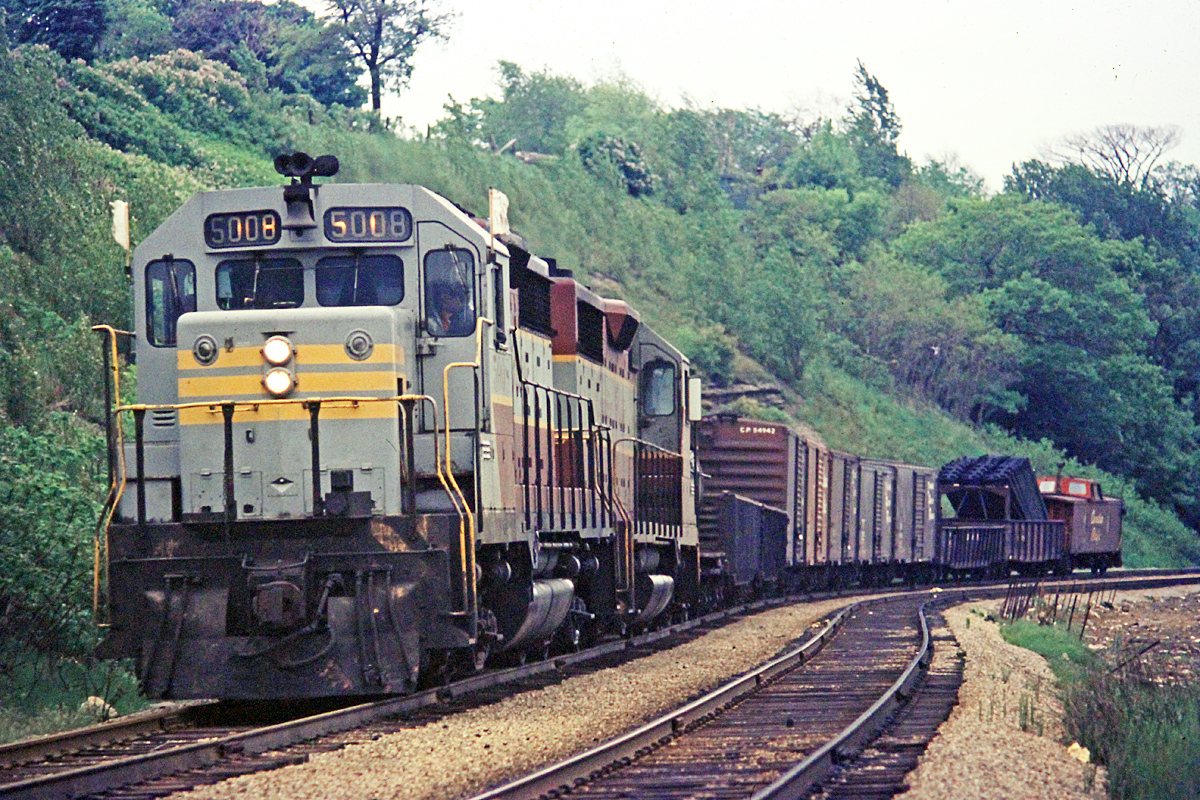 Flying "Extra Flags" CPR 5008 and another SD-40 haul a short train near the cemetery on York Blvd in Hamilton, ON.  The date is June 1968.  Note the unusual centre cupola caboose bringing up the tail end of this train.
