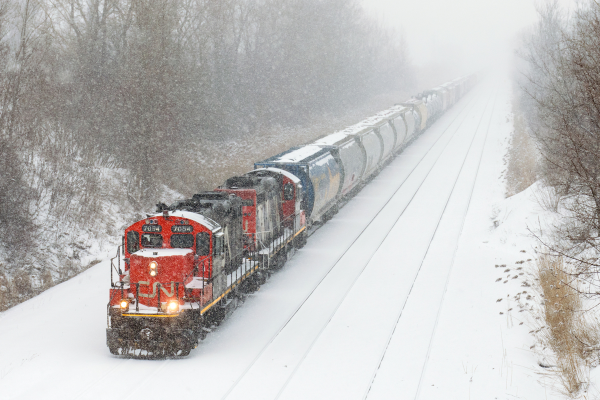 I could hear it coming a mile away. With heavy snow falling in Montreal this afternoon, visibility was not great. I saw a train lined westbound on the freight track of CN's Montreal Sub and I heard it well before I saw it, with two GP9's (CN 7054  & CN 4102) giving it all they've got to bring 75 cars into nearby Taschereau Yard.