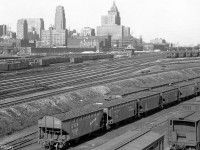 The downtown Toronto Skyline and railway corridor is pictured looking east of the Spadina Avenue overpass in 1950. <br><br>At the bottom right, Illinois Central, Louisville and Nashville, and C&EI hoppers are spotted at CN's Spadina Roundhouse, loaded with coal for the coaling tower and <a href=http://www.railpictures.ca/?attachment_id=24444><b>steam engines that populate the ready tracks</b></a>.<br><br>The passenger cars on the single-ended tracks in the upper right are in part of CPR's John St. coachyard near their roundhouse (out of view). In the distance on the upper right is Toronto Union Station and its train shed, the CN Express building, and the CN Telecommunications building under construction (later CNCP, Unitel, and presently the telecommunications hub at 151 Front St.). The main Toronto Terminals Railway tracks to/from the station pass through the middle of the image, along with the TTR's John Street interlocking tower that controlled train movements in and out of this area (one of 4 TTR interlocking towers around Union).<br><br>Toronto's 1950 skyline was devoid of office towers and condos that would spring up in the decades to follow. The CPR's Royal York Hotel and the Canadian Commerce Bank Building (the tallest building in the British Commonwealth at the time) are the two most prominent buildings. Also visible on the left are CN's old freight sheds north of Front Street near Simcoe, and CN's lower freight yards with loading platforms and team tracks full of boxcars and other equipment.