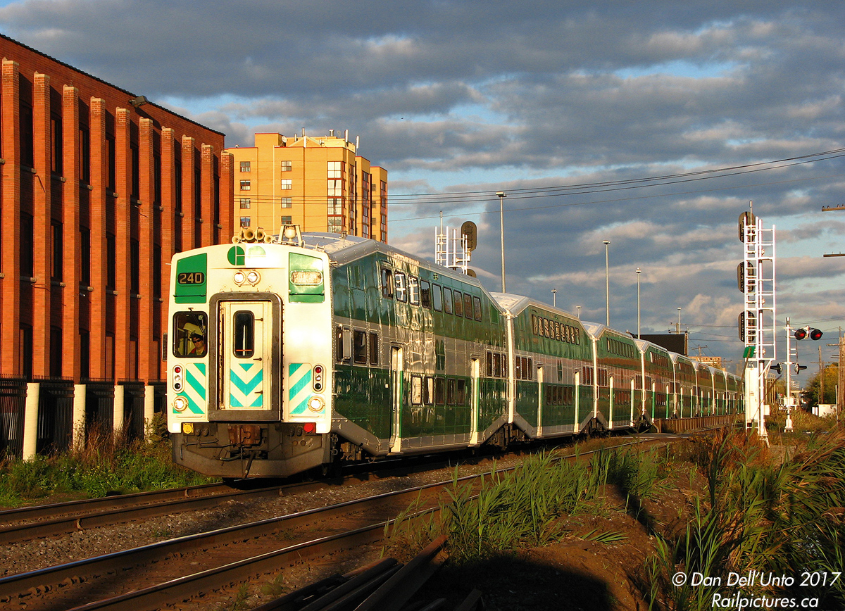 GO Transit UTDC cab car 240 (still sporting its original unrebuilt single window cab) heads Georgetown-line train #207 out of Brampton Station, across Mill Street crossing and through the then-new signal light towers, about to hammer Brampton diamond (just behind the photographer). Eager commuters from Toronto, hidden by the train, await its passage before crossing the tracks and walking to their cars in the "south lot" by the Dominion Skate building.