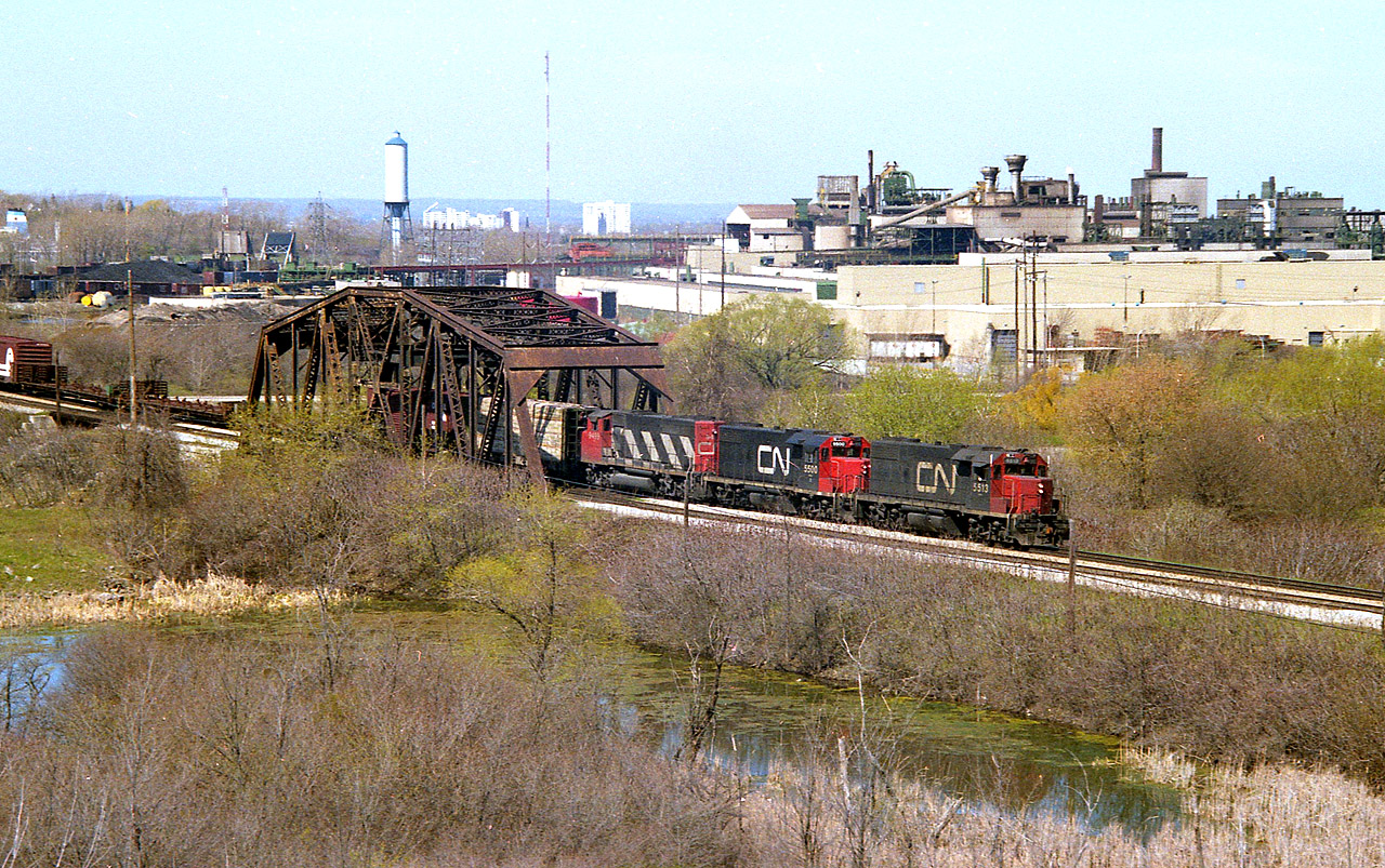 A favourite shooting place that was, in my own mind, underutilized. Just didn't have the time, and it wasn't long after discovering this spot that it became overgrown and off limits. It is now fenced off private property of Walker Industries (Quarries) But I did get a couple of nice shots here....a spot initially located as I was trying to find a scene for the start up of AMTK thru Niagara that would not be duplicated by other photographers. And succeeded. In this shot, CN 5513, 5500 and 9499 are Niagara-bound thru 'CN Iron Bridge'. The sprawling Glendale Av GM plant dominates the background. Two GP38-2 and a GP 40. I loved that plain black with white noodle scheme for some odd reason.