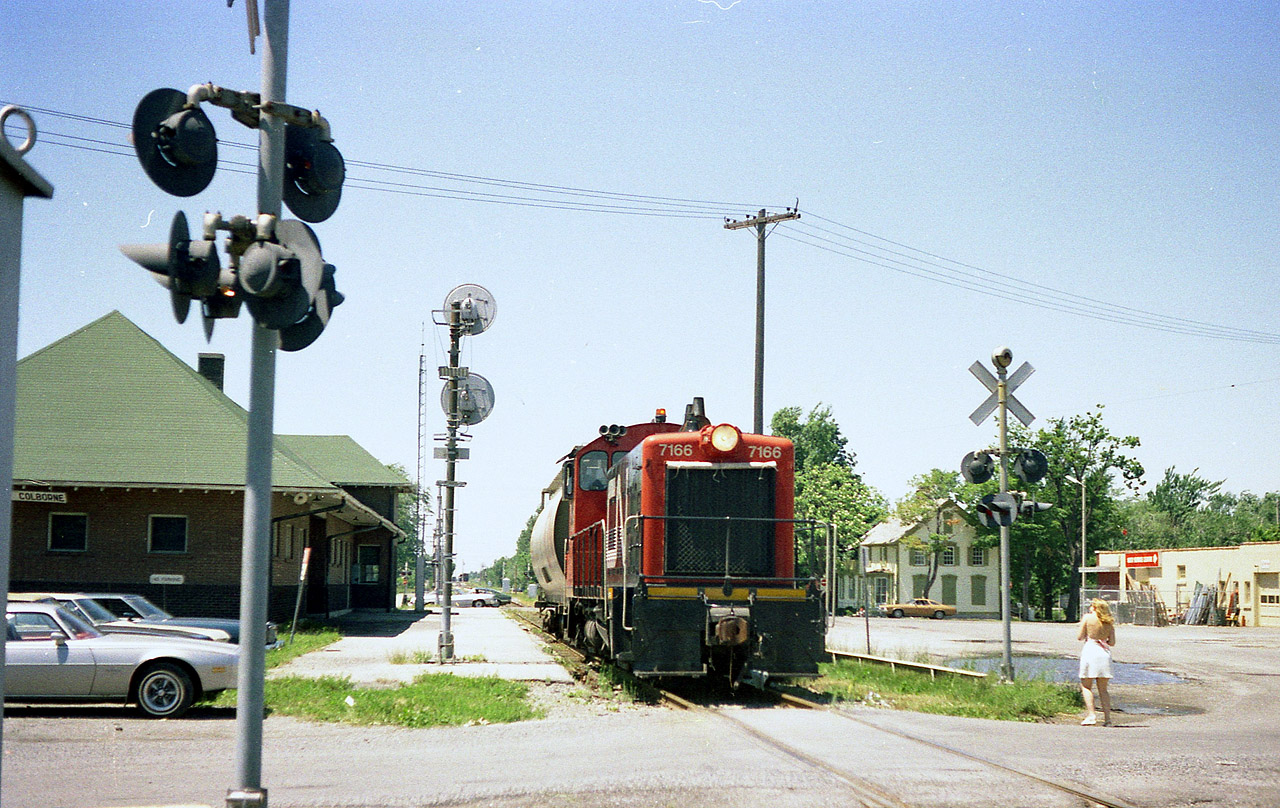 It is a rather hot July 1st, and CN 7166 is about to cross over the canal via Bridge 20, to fetch a few loads.
The Sidekick has just grabbed a shot of the unit passing CN Port Colborne station so we've got this move covered. (she earned her keep)  Bridge 20 was removed 20 years later, and the track was realigned curving north thru the pavement on the right, running now up the west side of the canal.