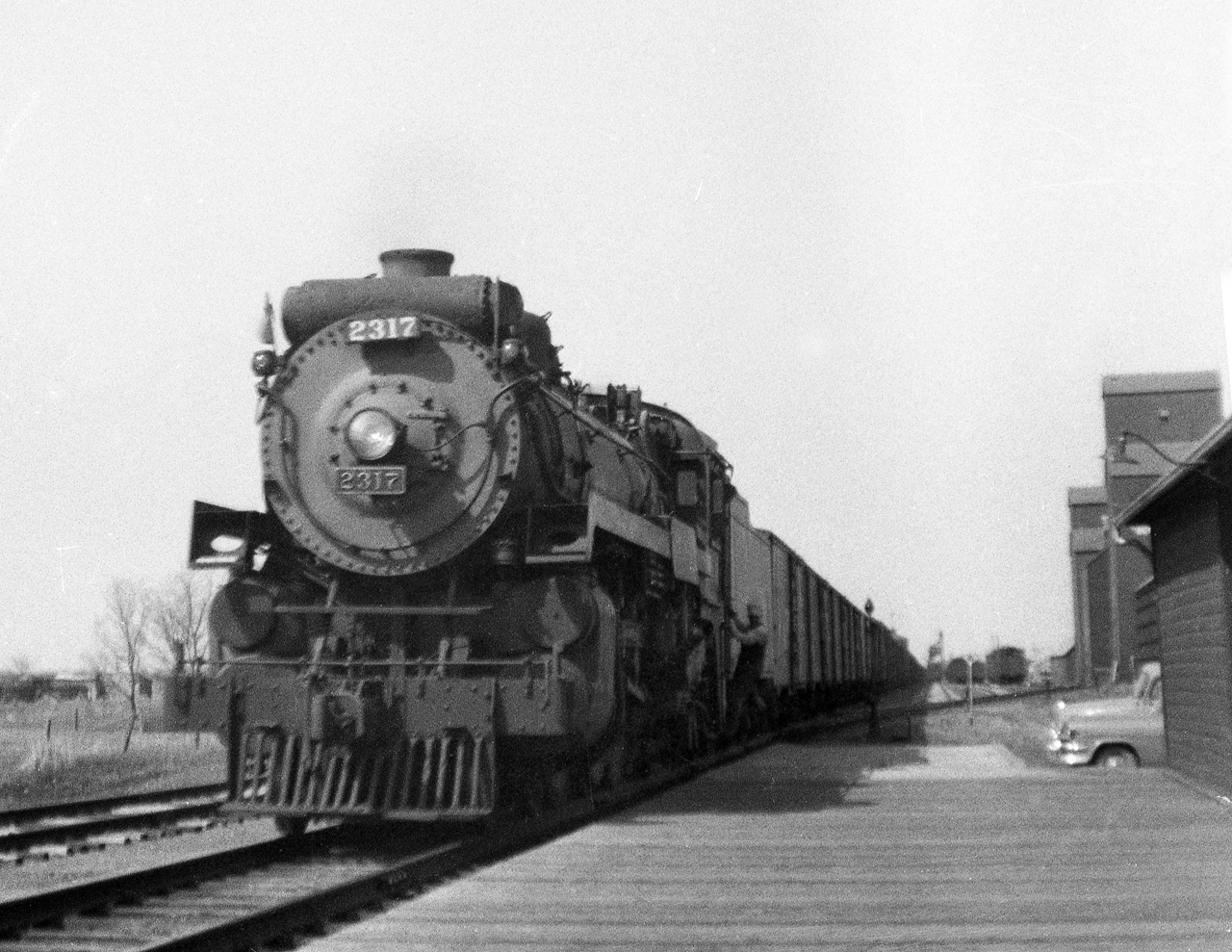 After walking train while G3c 4-6-2 2317 took on coal and water at the west end of town, the conductor gets off at the station to fill out the train register. In the steam era grain moving from southeast Saskatchewan moved from Weyburn via the Kisbey and Arcola subdivisions through a terminal at Souris. The 2317 is preserved at Steamtown in Scranton Penn.