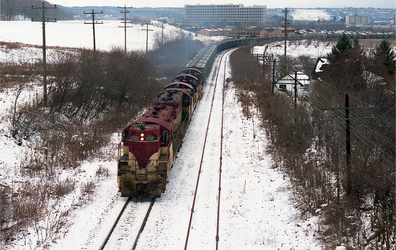 A TH&B "Rock Extra" always got the fans worked up. Here is a classic run with TH&B 72, 73, 57, 51 and 55 working hard to climb the escarpment to Vinemount. I'm standing on the road-bridge where old Hwy 20 passes over the tracks; a place now that is off-limits to train watchers. I suppose one could still venture to this location, but parking has been removed, barriers are up, the road is 4 lanes of heavy traffic, and getting to finish off your days on this green earth as roadkill is an extreme possibility. There were a number of rock trains in the 80s, heading to Port Maitland for the most part, and the very sparse TH&B roster was squeezed to the limit, resulting in yard switchers assisting to ensure the train made it with fewer problems to the crest at Vinemount. Then excess puller-power returned to Kinnear. This head end consists of two GP7s, and two SW9s with an NW2 (#51) between. The #51 went to the OSR in Salford back in 1992. They still have it.