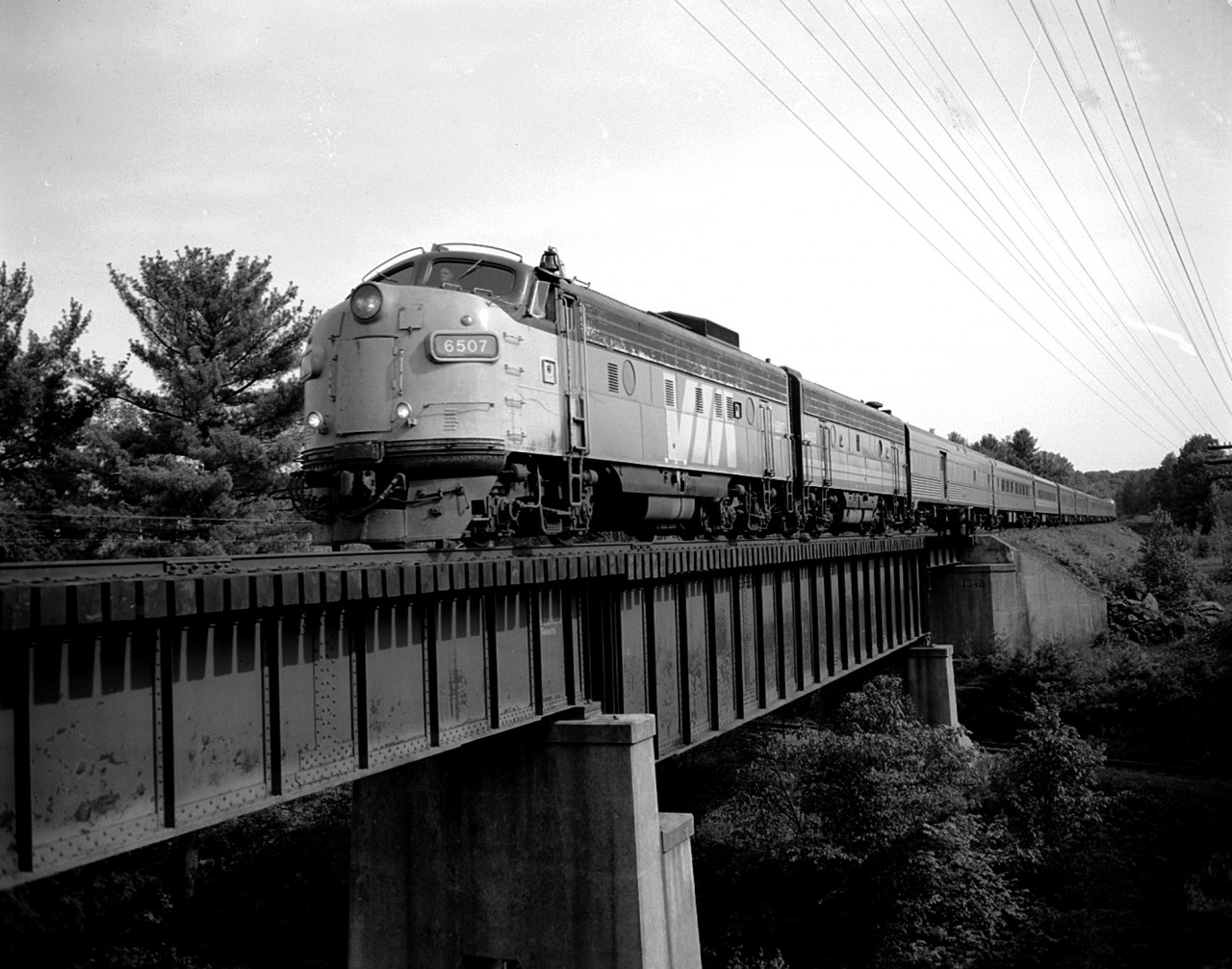 The VIA up from Toronto is running a little bit late this day. Time is around 1800 rather than the 1715 it normally pulls in at CN Boyne. Every minute helps. Gives more light to the nose of the leader:o)as the late day sun swings around. In this B/W view VIA 6507 and 6622 are seen crossing the bridge over the valley where the former line out to Parry Island and Depot Harbour used to run. Now, like in most other pulled up lines, is has been converted to a walking trail.(the line was pulled up fall of 1987)
This image is from a scanned 4x5 negative, 400 ISO shot at 200f8 with the Speed Graphic.