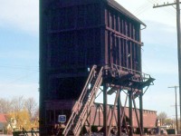 Steam engines required more frequent fueling stops for coal and water than diesel, and as a consequence structures had to be set up at various junctions, terminals, and outlying points to supply them when running low. After the steam era ended so did their usefulness, and most were demolished in the following years.
<br><br>
The coaling tower pictured here is in Guelph at Canadian National's Guelph Junction, located by Crimea and Alma Streets. A pair of CN hoppers are spotted below the tower with "blue flag protection" applied, where they dump their coal into a pit under the track (note the piles of coal on the ground around the hopper bays), which is then scooped up into the tower via a conveyor system and deposited inside, waiting to be dumped into steam engines via the chutes located around the platform.
