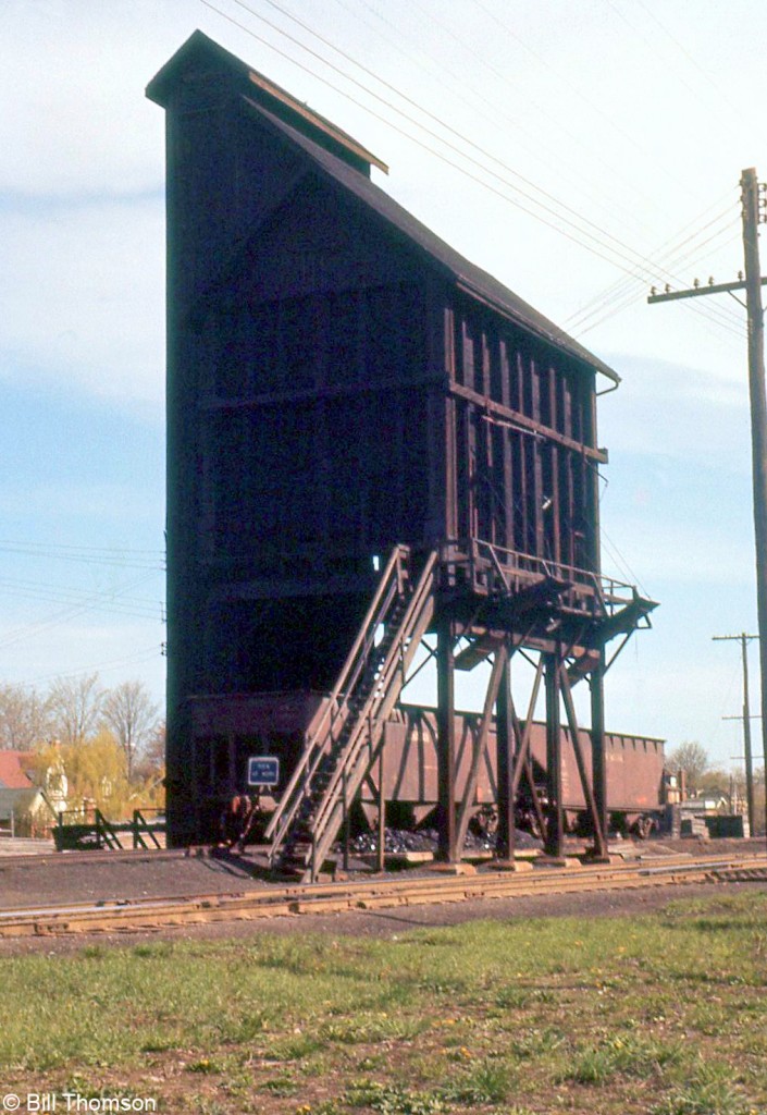 Steam engines required more frequent fueling stops for coal and water than diesel, and as a consequence structures had to be set up at various junctions, terminals, and outlying points to supply them when running low. After the steam era ended so did their usefulness, and most were demolished in the following years.

The coaling tower pictured here is in Guelph at Canadian National's Guelph Junction, located by Crimea and Alma Streets. A pair of CN hoppers are spotted below the tower with "blue flag protection" applied, where they dump their coal into a pit under the track (note the piles of coal on the ground around the hopper bays), which is then scooped up into the tower via a conveyor system and deposited inside, waiting to be dumped into steam engines via the chutes located around the platform.