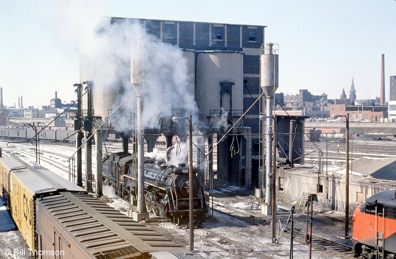 Canadian National's large coaling tower at Spadina Yard in downtown Toronto, used in the steam era for fueling the many large and small steam engines based out of the roundhouse, continued to exist for years after steam was retired. CN Northern 6167, enjoying its brief second career in excursion service, is pictured underneath it while receiving sand from the modern sanding towers installed nearby. Bathurst North Yard just south of Front Street can be seen in the background full of freight cars (long used as a CN freight yard until being repurposed to store GO trains). The nose of an FP9 can be see on on the right, and on the left are some early CN 50' yellow mechanical refrigerator cars.