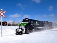 <b>Crossing closed for the winter.</b> A Société du chemin de fer de la Gaspésie windmill train (which consists of 72 flat cars holding 48 windmill blades, as well as 1 loaded woodchip car up front) is  rounding a curve in the small town of Carleton-sur-mer. The crossing it is approaching is closed for the winter and is very snowed in.