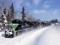 The Société du chemin de fer de la Gaspésie's windmill train is passing through the town of Escuminac, on its way to Matapedia and interchange with the CN. Power is three ex-CP RS-18's, two which have been repainted into an SP Black Widow-inspired paint scheme.