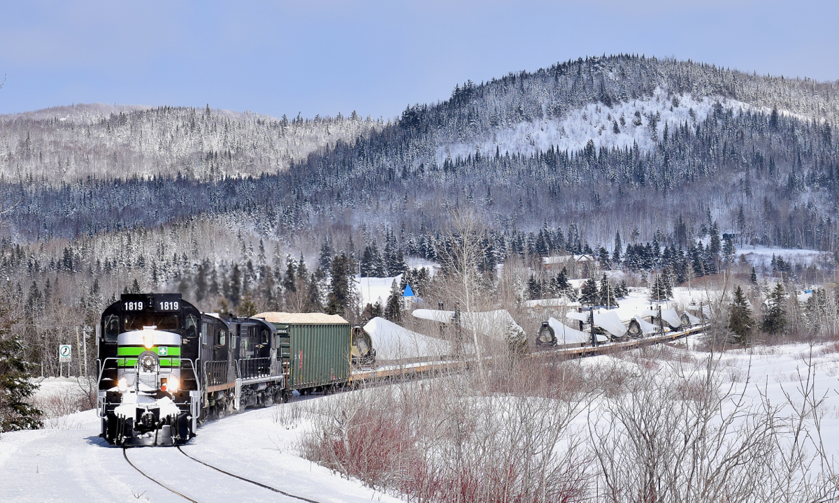 Three ex-CP RS-18's (two recently repainted into an SP Black Widow-inspired paint scheme) lead a train consisting of 72 flat cars holding 48 windmill blades (as well as 1 loaded woodchip car up front), as it rounds a curve along the Restigouche River, headed for nearby Matapedia and interchange with the CN. These windmill blades are destined for Texas and represent a new business for the Société du chemin de fer de la Gaspésie, which runs this scenic ex-CN line.