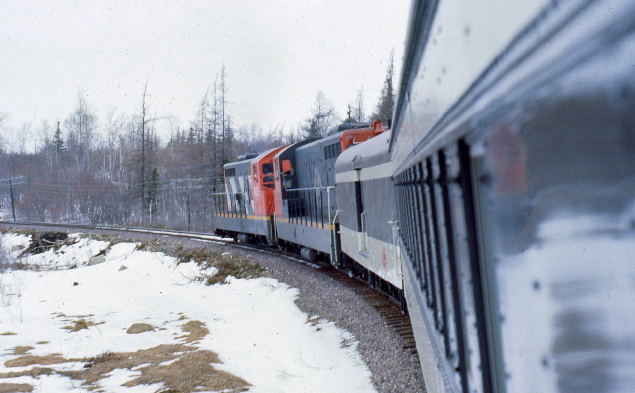 UPGRADE AT CRUISERS. Terra Transport Mixed Extra 935 West has just crossed under the TCH overpass in Bishops Falls on April 16, 1988 and is climbing upgrade at Cruisers Brook, said to be the steepest grade on the entire 547 Mile Newfoundland Railway. Departing Bishops Falls at 11:00 AM, the two NF210's (935 and 927) leave with passenger only equipment (Baggage 1308 and Coach 764) until four container units were picked up in Grand Falls. The only travellers to make the entire 138 mile journey to Corner Brook were the photographer and his friend Paul who was delighted to experience his first ride on a Newfoundland train. One other, a cabin owner, got on at Millertown Junction and soon departed in several feet of snow at Gaff Topsail. The hospitality and friendliness of the Newfoundland crews were beyond compare, with conductor Carl Dillon inviting us both back to the caboose and allowing us to ride in the cupola for several dozen miles.