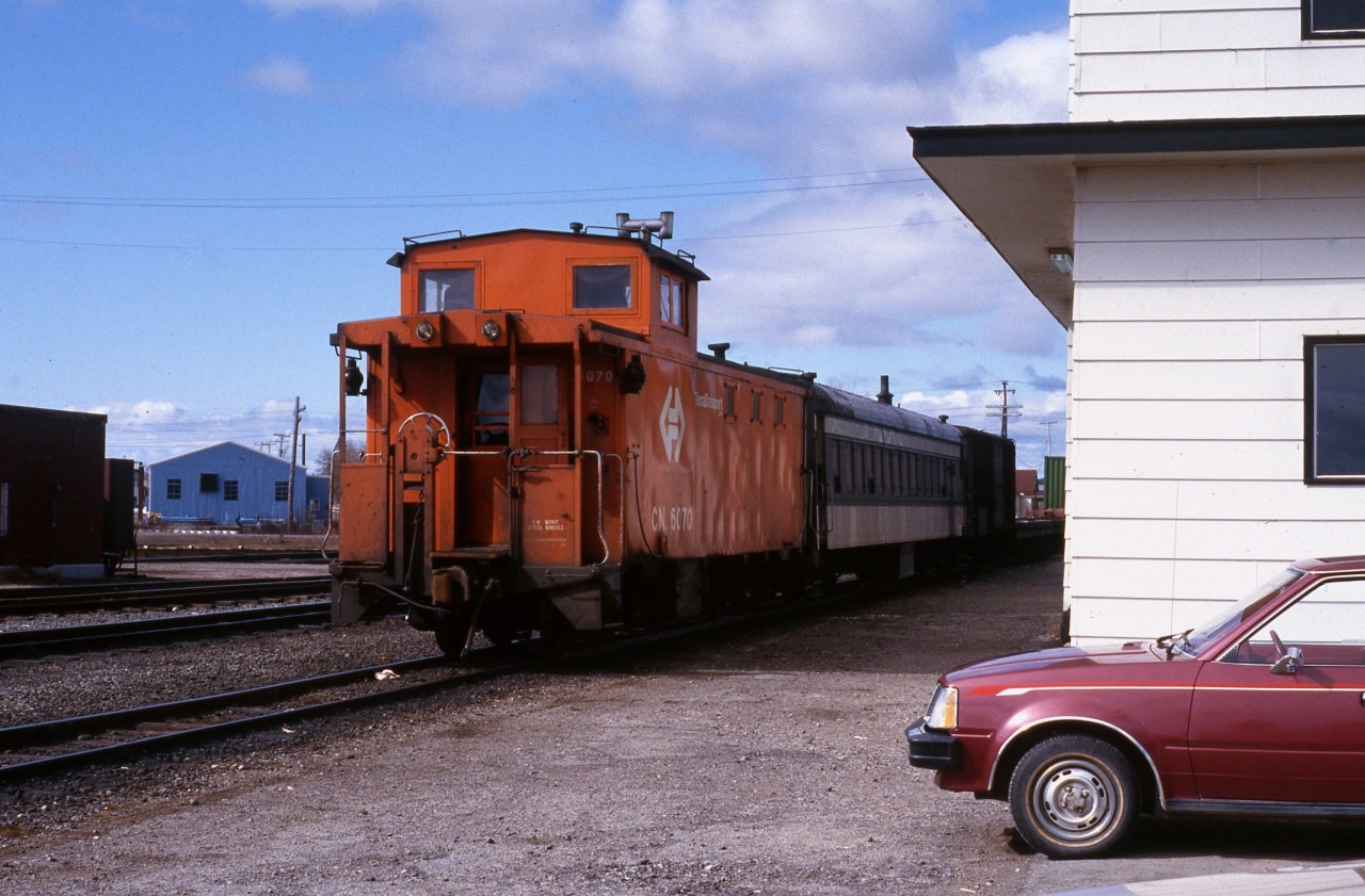 DEPARTING BISHOPS FALLS. Terra Transport Caboose 6070, built in 1967 by National Steel Car of Hamilton for CN's narrow gauge Newfoundland division, is tacked to end of Mixed Extra 945 West on April 20, 1987. Upon learning that a mixed train service still operated on the Island railway, the photographer and his then girlfriend (now wife) left the capital city of St. John's to eagerly ride what was he believed was lost forever. Next to the caboose was coach 757 in which the two were the only passengers for the entire 138 mile journey to Corner Brook on that beautiful spring day.