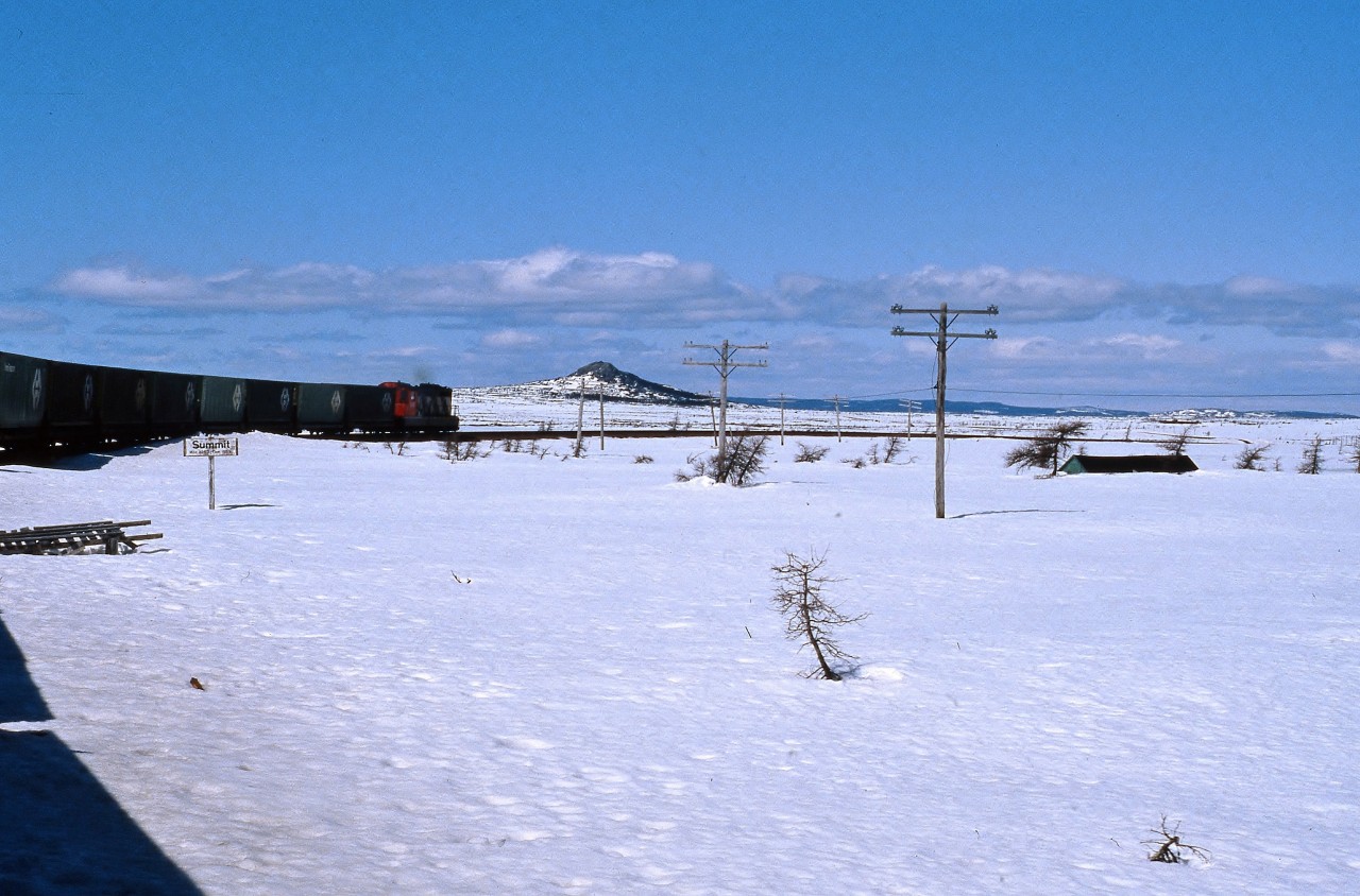 REACHING THE SUMMIT - Terra Transport Mixed Extra 945 West reaches Summit on April 20, 1987. At 1550 feet above sea level, it is the highest point of the 547 mile narrow gauge Newfoundland Railway on the entire  mainline. With the roof of a cabin barely visible, the heavy snowfall from the winter is still piled several feet high, belying the fact that spring is well underway elsewhere on the Island. The only passengers to travel there that day were the photographer and his then girlfriend (now wife) on their very first trip on a Newfoundland train.This image and it's modern day counterpart can be seen in my first book, RAILS ACROSS THE ROCK - A Then & Now Celebration of The Newfoundland Railway (2013) published by Creative Book Publishing.