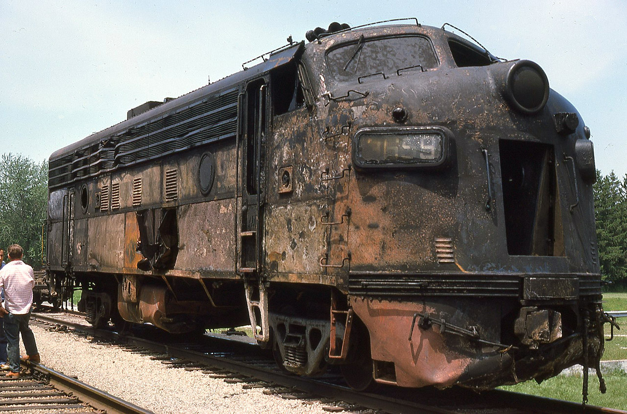 On the morning of June 10/75 N&W train DN90 suffered a broken traction motor gearcase cover while moving at track speed through Simcoe on the CN Cayuga Sub. The resulting derailment caused lead F7 3659 to plummet off the Highway 24 bridge and burst into flames, killing the crew. Trailing unit 3725 derailed but remained upright. Two days later, on my lunchhour break from TH&B Brantford office duty, I drove to the aftermath and shot 3659, after it had been retrieved from the overpass and set aside in preparation for movement.
