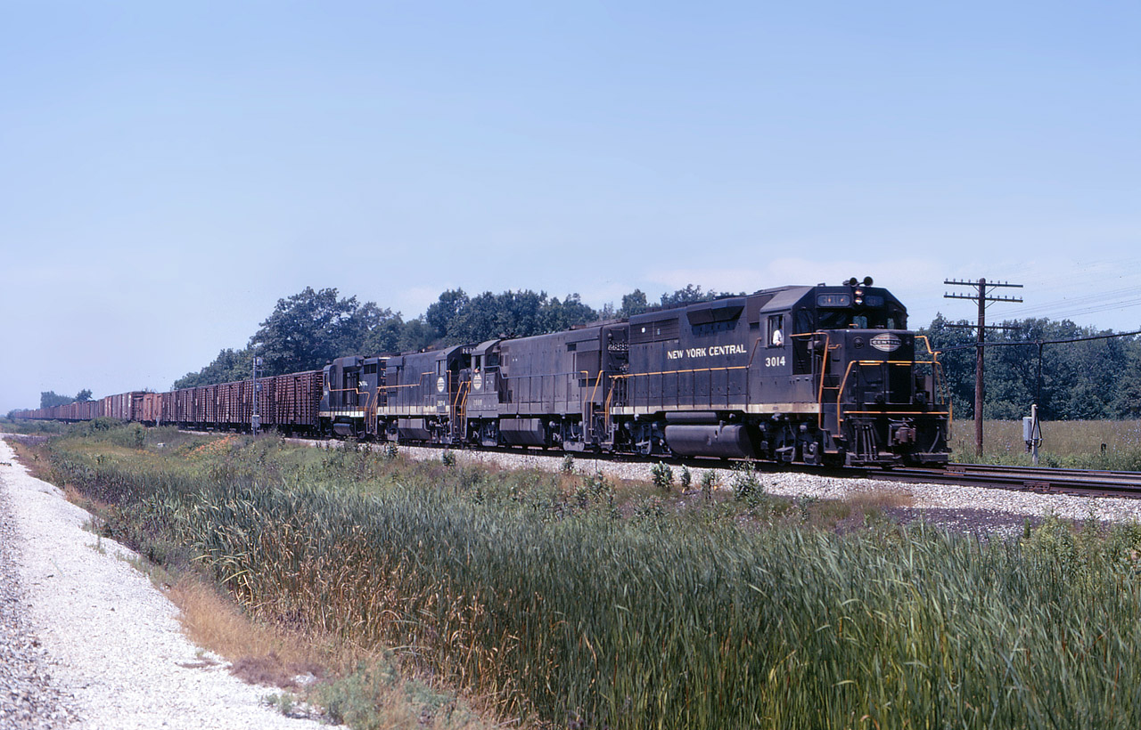 July 1968 Penn Central train NY-4, Chicago to New York City is about to hammer across the diamond at Canfield.  GP40 3014 along with U30B’s 2888-2874 and a GP30 have livestock and refrigerated goods as they hurry to make the next morning cutoff times for the Big Apple markets. It is only 6 months since PC was created and none of these engines have been restencilled. Looks like a cloudless humid day at The Junction, you can probably listen to the rail joints bang as the heat induces the track to expand
