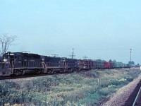 Sept 1968, an early evening finds Penn Central westbound train ML-9 ( Multi Level) passing through Canfield on the Canada Division. This train originated at Framingham MA with a day’s worth of empty racks going back to Detroit region facilities for reloading.  A GP40 and a pair of U30B’s can easily handle this train with their combined 9,000 hp but the draft created will stir up the dust and make those weeds wave back & forth for a few minutes.  That wooden property line post in the middle of the bullrushes once had CSR painted on it (Canada Southern Railway).