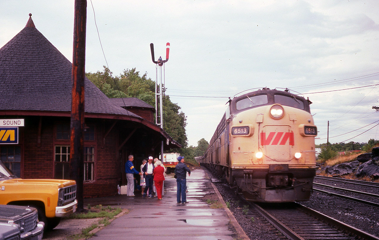 VIA #10 slows for a stop for a couple of passengers to board as well as a couple to detrain at the old CP station which was once a popular stop. This building still exists, by what seems like a miracle, as it was closed for many years and at the mercy of the elements and the vandals. But it survived, and is now home to an attractive Art Gallery. And has been remodeled inside out. Photo ops here now are tight, there is a wrought iron fence protecting visitors from the trains; there is no more siding nor yard with just the mainline now to be seen. Back in the 70s & 80s it was a great place to hang out, even in the rain ! Power on this Toronto bound train today is VIA 6513 and 6624.