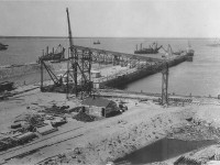 During construction of the Churchill grain elevator, 0-4-0 #8 pushes what appears to be a stationary boiler under a tarp. Judging by the number of workers around, there must be a problem. The large steel frame is for the conveyor from the elevator out to the pier for loading boats. The travelling crane erecting the frame has a pair of booms and has a boiler in the corner. Photo taken by my grandfather from the roof of the powerhouse with editing assistance from the moderators.