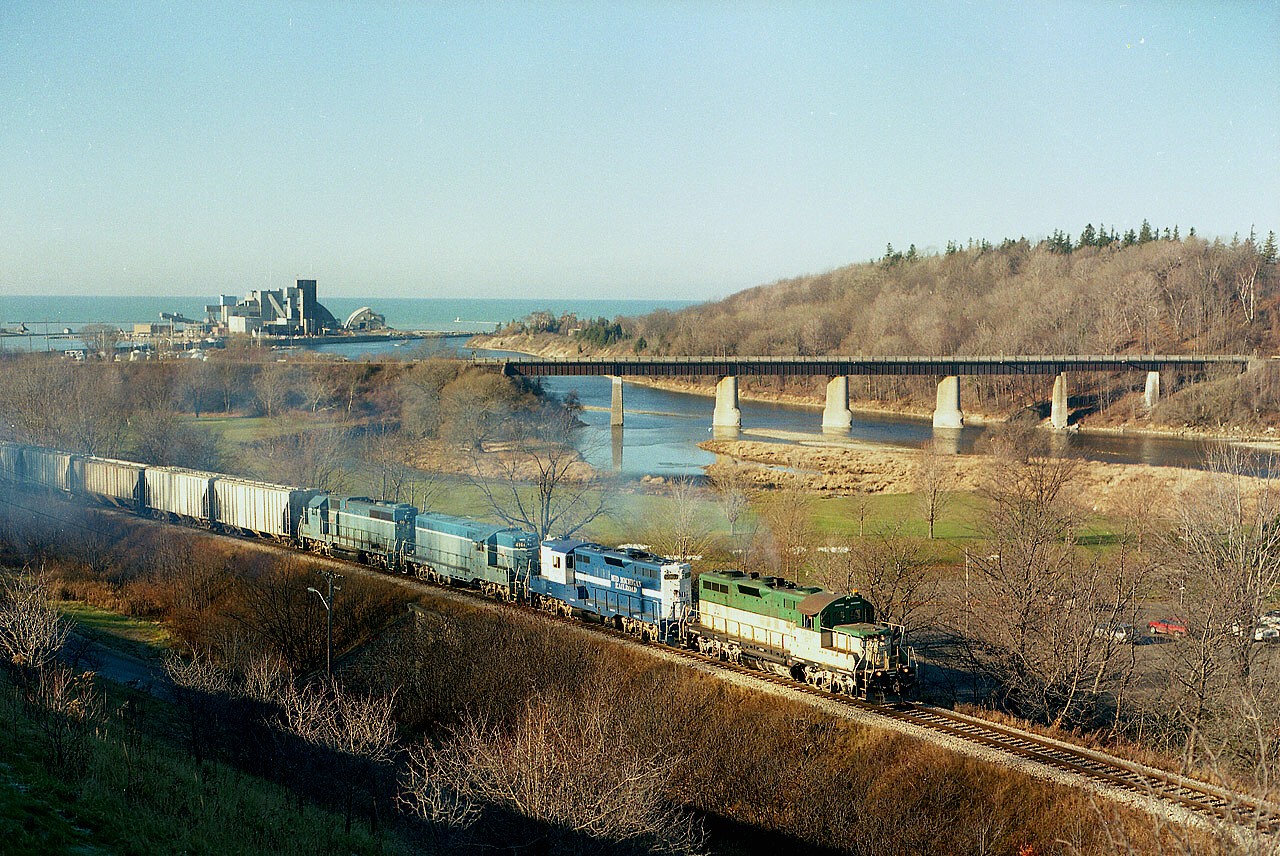 An old once familiar scene at Goderich. GEXR 177, Mid-Michigan RR 5967, GEXR 4161 (slug), GEXR 66 (slug mother) drag a load of salt up from the Sifto Salt complex seen on the shore of Lake Huron in the background. The bridge over the Maitland River is the former CP connection to the town, now used as a hiking trail. The CP up and left about 10 years prior to this photo being taken. I believe all locomotives in this image were scrapped in 2008.
The MMR 5967 was loaned to GEXR on 10/97 and departed for CBNS in early 1998, so this was a bit of a rare catch.