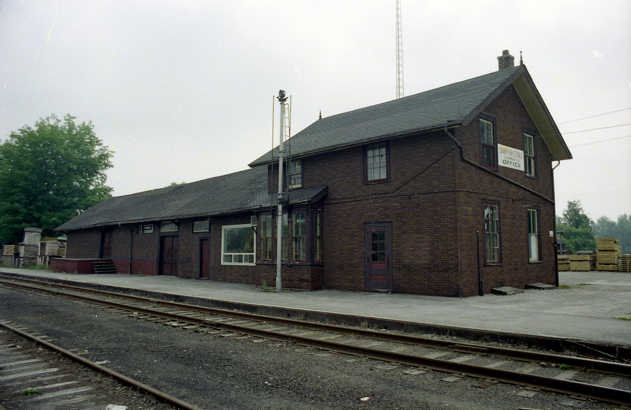 There is no railroad in Tweed any more. Once upon a time the Bay of Quinte Rwy served the community. Also CP from Glen Tay in the east (near Perth) ran right thru town to Havelock. Tweed to Glen Tay was taken up around 1972, and the Tweed-Havelock connection was history by late 1987, and that was the end of the line here. Lumber was a big business in this part of the province, and it relied on the railroads back then. Sawyer-Stoll was a wide spread name in the industry. Over the years competition forced this company to retreat, and so they consolidated at the old CP station at Tweed. (Sawyer-Stoll was bought out in 1979 by G.W.Martin) In later years, images show this station much shorter, as not long after this photo was taken the freight section was removed up to the door to the office with the new window replacement is seen. The old building, constructed around 1884,and no doubt outlived its usefulness, was demolished in 2008.