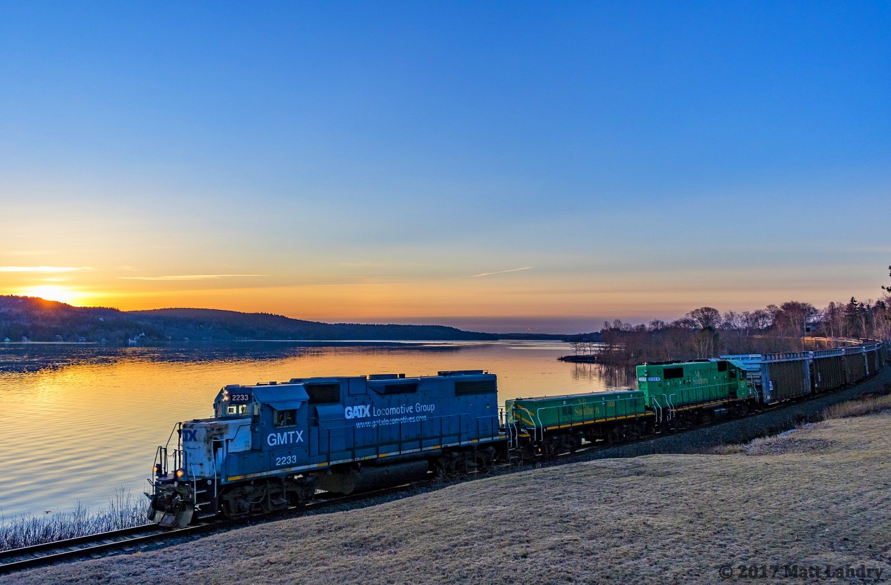 With the sun on the rise along the Saint John River Valley, GMTX 2233 leads an extra westbound 907, as they run along the Saint John River at Grand Bay-Westfield, New Brunswick. A steller lashup, with slug 008 and NBSR 2318 making up the rest of the consist of this empty woodchip train.