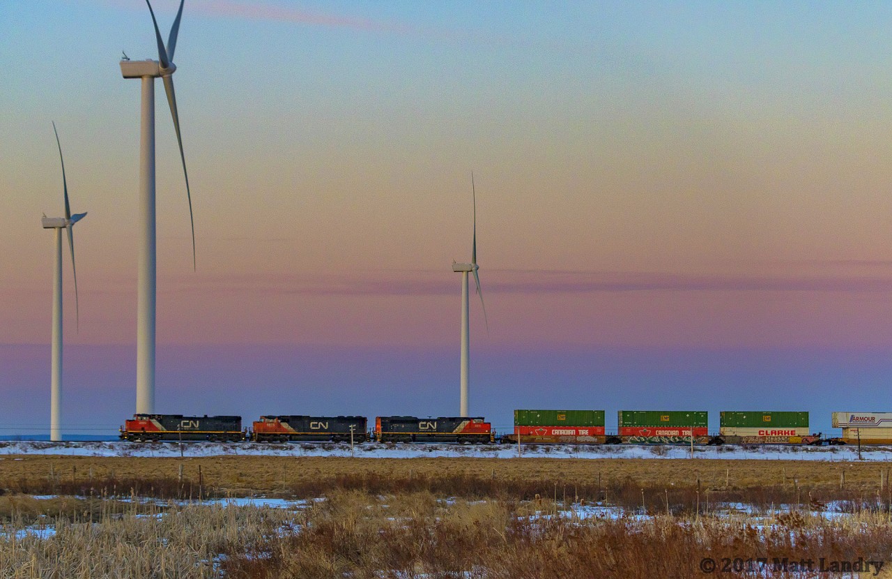 With the sun just starting to peak over the horizon, IC 2699 leads eastbound stack train Q120, as they pass the turbines on the approach to Amherst, Nova Scotia.