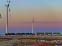 With the sun just starting to peak over the horizon, IC 2699 leads eastbound stack train Q120, as they pass the turbines on the approach to Amherst, Nova Scotia.
