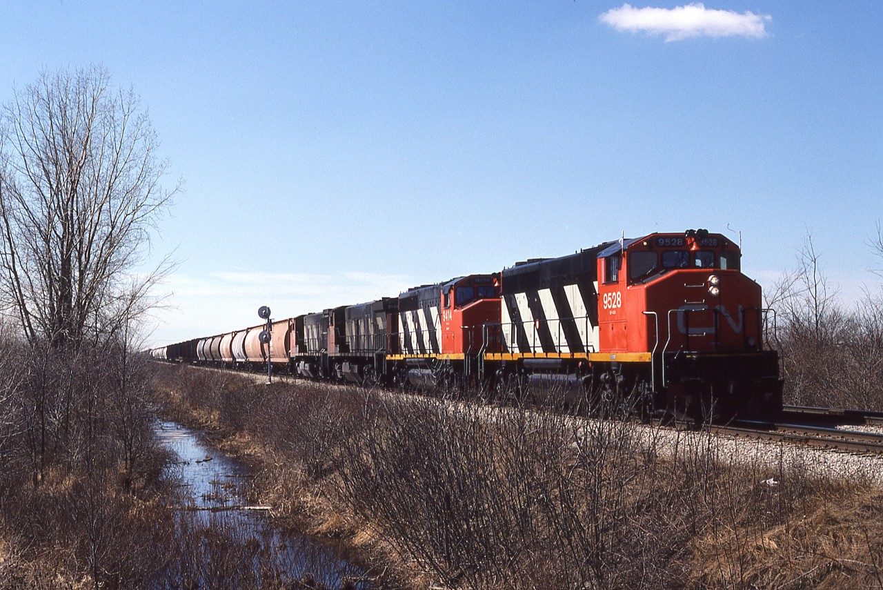 Windsor-Toronto manifest 422 with it's usual heavy consist is about to cross the CP Windsor Sub. diamond west of Chatham in March 1987. Two GP40-2W's and two M420W's have salt loads and other mixed freight behind them as they hustle their way eastward. At the rear of the train are loaded auto racks from Chrysler that will be re-arranged at Toronto to go both east and west to their Canadian destinations.