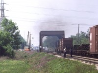 Ho hum, another day of wearing the white hat and making decisions.
I'm standing at the Sass Road crossing, recording the passage (and not-so-perfect meet) of NS train 27 with VIA number 74. Unfortunately I was not able to get the engines passing one another on this attempt, at this location. But what I did get shows a cross section of activity.
Train 27 with a pair C30-7's did not have any elevator switching to perform at Thamesville this day, so his train makeup is entirely automotive related. After passing my location, he is about to accept the CLEAR signal at the C&O diamond, as witnessed by the double greens on the dwarf signal, just ahead of the lead unit.
The high green signal is the Clear train order board at Chatham East. And except for the two fellows nearest my lens, all other personnel are standing off to the south of the eastbound main as VIA 74 looms in the distance.
Taken with a Hanimex 300mm mounted on a Canon FTb.