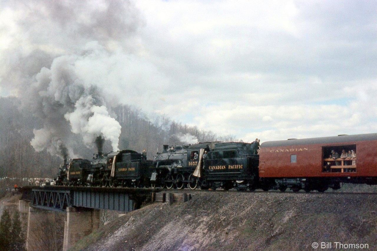 The famed CPR steam triple header is seen on the long curving bridge at Forks of the Credit, on May 1st 1960. Smoke is wafting backwards as the power is backing the train up, and photographers line the north end of the bridge for a runby photo shoot.Excursion engine CPR 136 at Orangeville Yard: http://www.railpictures.ca/?attachment_id=28543Tripleheader consist arriving in Orangeville: http://www.railpictures.ca/?attachment_id=28312