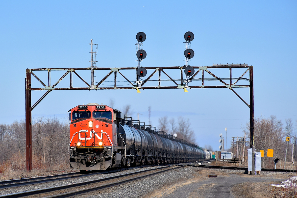 The last time I shot a westbound train under this signal bridge at Coteau there were 3 sets of signals for 3 sets of tracks. Since then the Ottawa Freight track and its corresponding signals have been removed at left. Here CN 377 speeds under the modified signal bridge with CN 2230 at the head end (and CN 8806 mid-train).