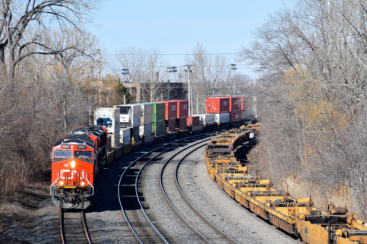 CN 3064 leads three other AC units (CN 3021, CN 2820 & CN 8100) as CN 120 rounds a curve in Ville St-Pierre. At right is a long string of empty well cars on the freight track of the Montreal Sub.