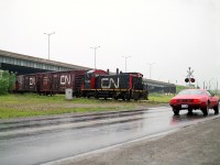 Ache!! Pouring rain. Regardless of the weather, catching a move on the North-End CN trackage was always worth going out. In this image, CN 7308 has just emerged from under the St. Catharines Skyway and about to cross Dieppe Rd. The two car train (plus caboose!) has just crossed Bunting Rd by the Canadian Erectors plant and is on the way to work NEI Parsons Ltd at 40 Neilson Av., which it will reach in a half mile after it crosses Bunting again. The line from Erectors northward has been lifted, and the remaining track is serviced now by Trillium. This SW1200RM, formerly CN 1373, as of 2000 went to Canac as their 7308.