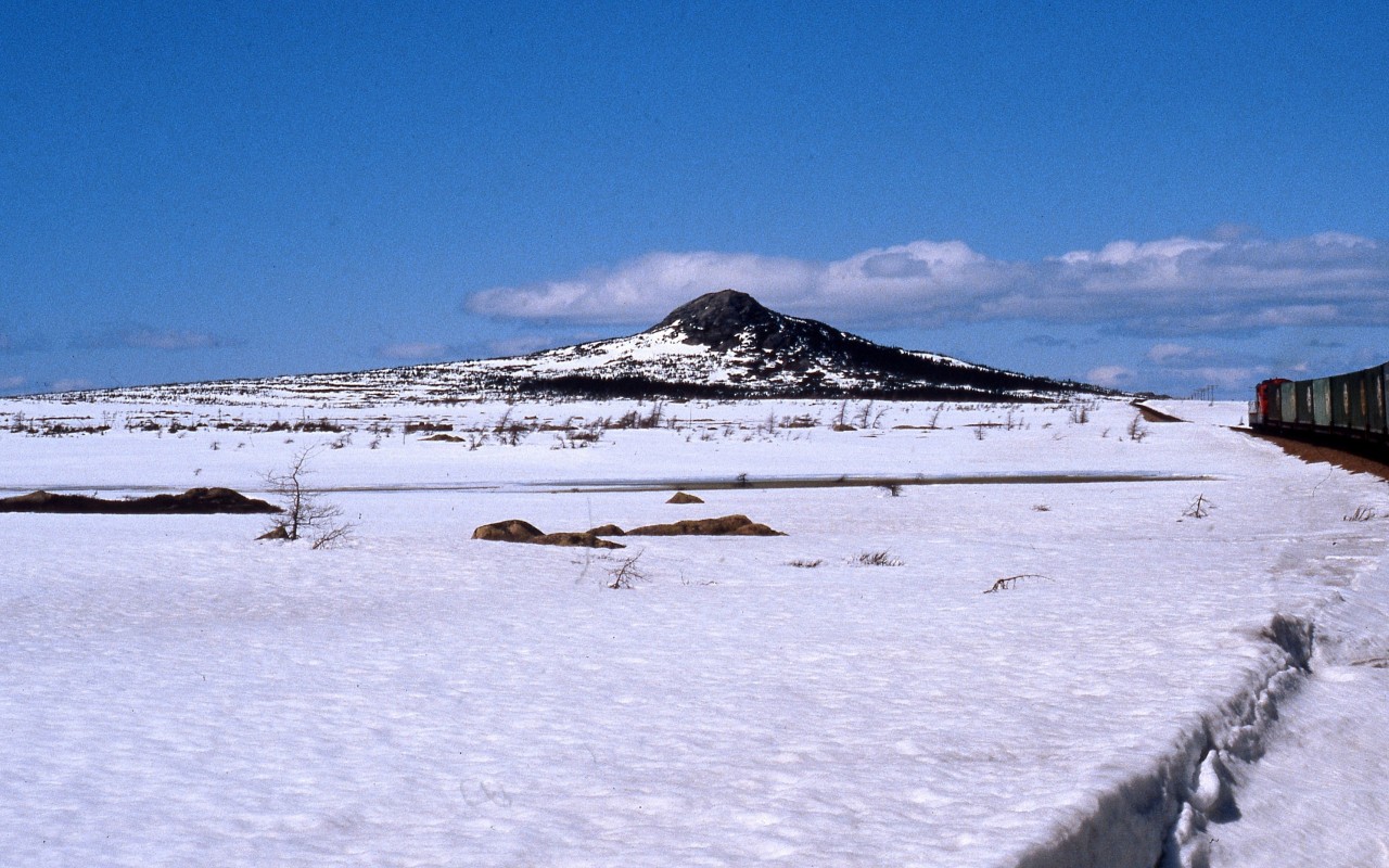 GAFF TOPSAIL - Terra Transport Mixed Extra 945 West approaches the hill known as 'Gaff Topsail' on April 20, 1987 while en route to the Flag Stop of the same name. Synonymous with Newfoundland Railway lore, the Gaff Topsail was one of four hills rising up from the plateau being named after the sails on a ship, the others being Main, Mizzen and Fore. Now just west of Summit, the train had already begun her 70 mile descent to near sea level at Corner Brook and the photographer and his girlfriend would continue to see wonderful vista such as this on their first Newfoundland train ride, making memories to last forever.