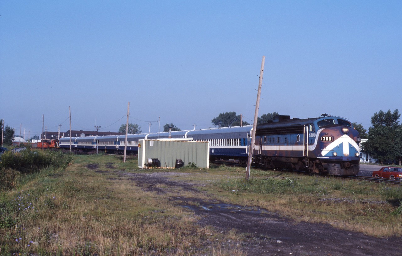 During the "Oka Crisis" in 1990, the Mercier bridge in the Montreal area was closed, causing traffic chaos. As a "relief valve", two commuter trains were temporarily operated between Montreal and St-Isidore over CN lines using former CP commuter equipment borrowed from West Island commuter service. Here we see Montreal Urban Community FP7 1300 passing through LaPrairie on the Massena sub. (Note the GP9 and van from the CN wayfreight in the background.)