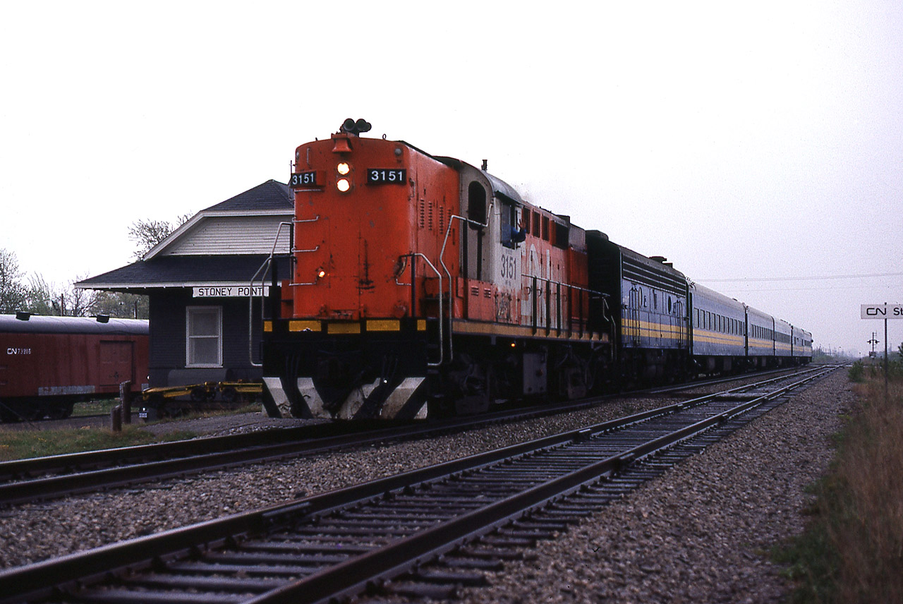 A Mike McIlwaine slide. VIA train 71 flies past the closed Stoney Point station on the final leg of it's journey from Toronto to Windsor. In deference to policy, the consist of 5 cars is being handled by 2 locomotives, but I'm sure there is an explanation. The 6 Tempo RS18's were not purchased by VIA, only leased for use in the Corridor. Wholesale changes were imminent as the F40's would be delivered starting in November 1986 and the Tempo cars would be sold off, replaced by dozens of second-hand ' heritage ' cars.