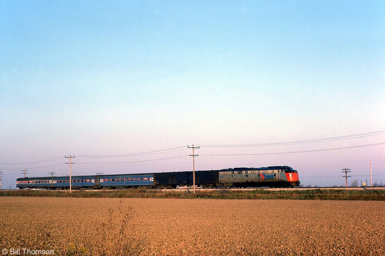 Amtrak's "Niagara Rainbow" heads eastbound on the Penn Central CASO Sub near Tilbury Ontario, on October 23rd 1975. A red-nosed silver EMD E-unit, a black ex-PC/CR baggage and three Amtrak-painted passenger cars make up today's consist.Note: geotagged location not exact.