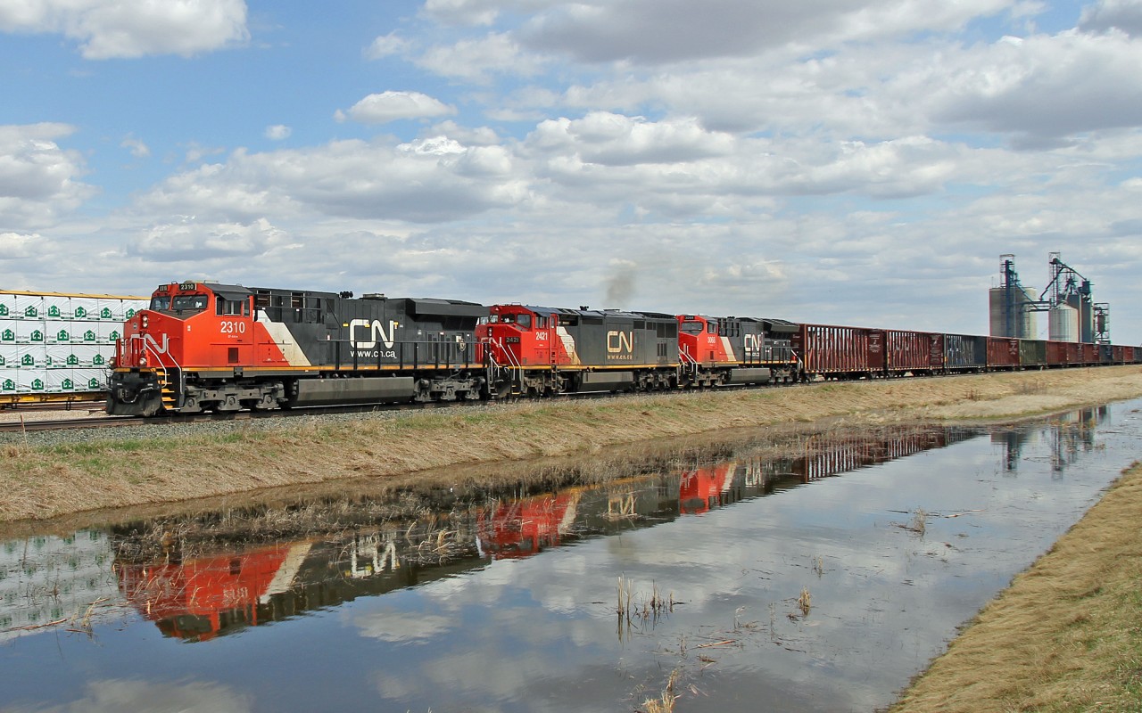 Meet at Viking.  ES44DC CN 2310, DASH8-40CM CN 2421 and ET44AC CN 3068 head empty lumber centre beams west past loaded lumber on the eastbound train.