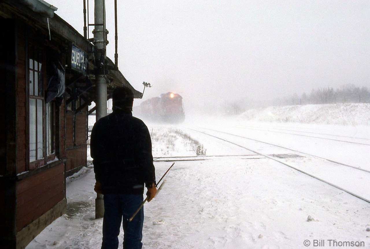 The operator at CP's Guelph Junction station stands at the ready, train order hoop in hand, to hoop up on orders to westbound CP #501 as it approaches the station during a snowstorm. This exemplifies the challenges operators had to deal with sometimes, passing on train orders in all types of weather in all seasons.

Hooping up orders at Guelph Jct to the westbound Pick Up: http://www.railpictures.ca/?attachment_id=16593